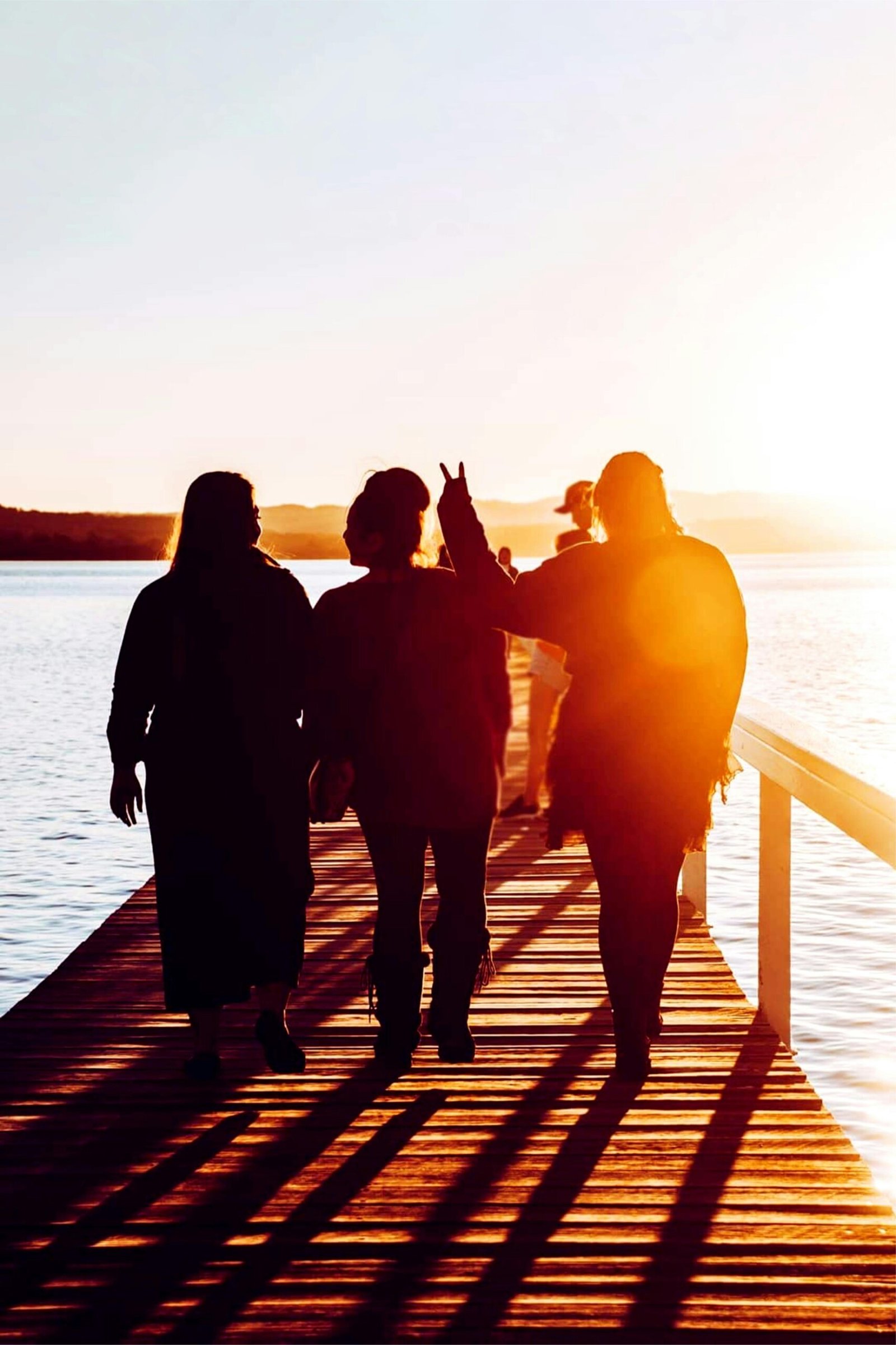 Group of friends walking on a wooden boardwalk during a vibrant sunset at Long Jetty, Australia.